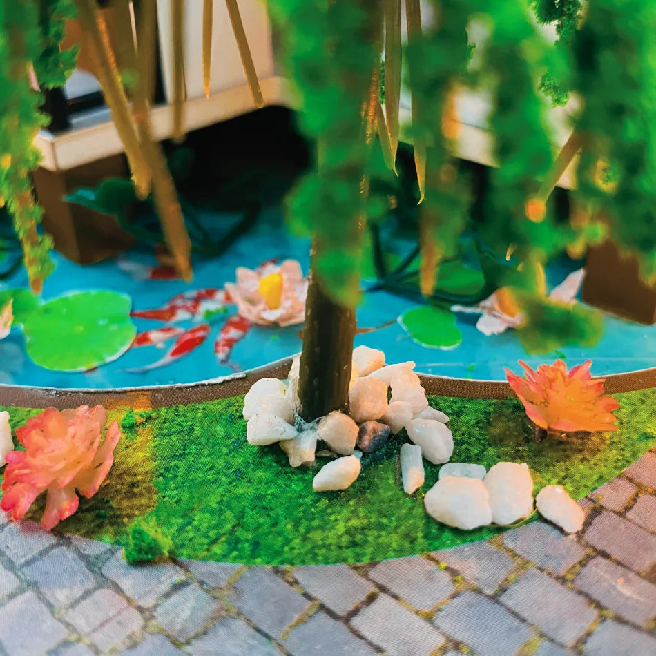 Miniature garden scene with pond, flowers, and stones on a blurred background