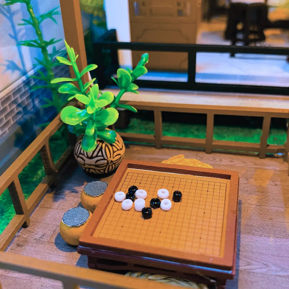 Go board with black and white stones on a wooden table, with a plant and TV in the background.