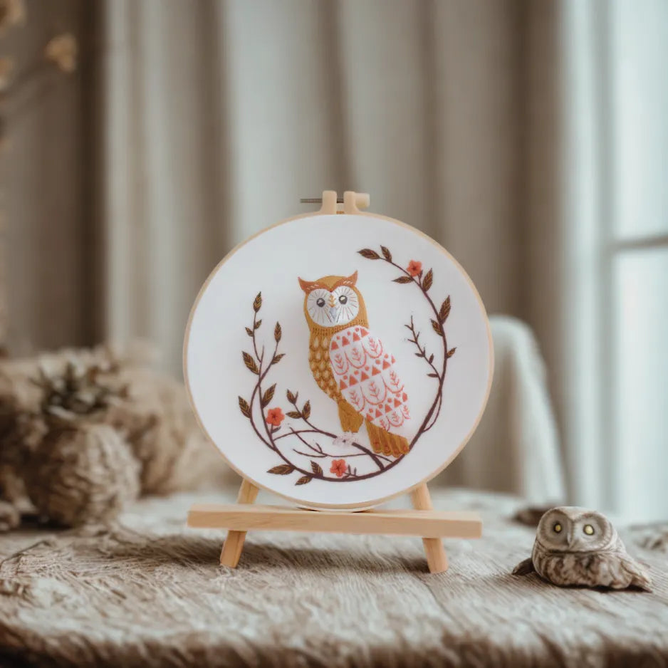 Embroidery hoop with owl design on a wooden stand against a neutral background