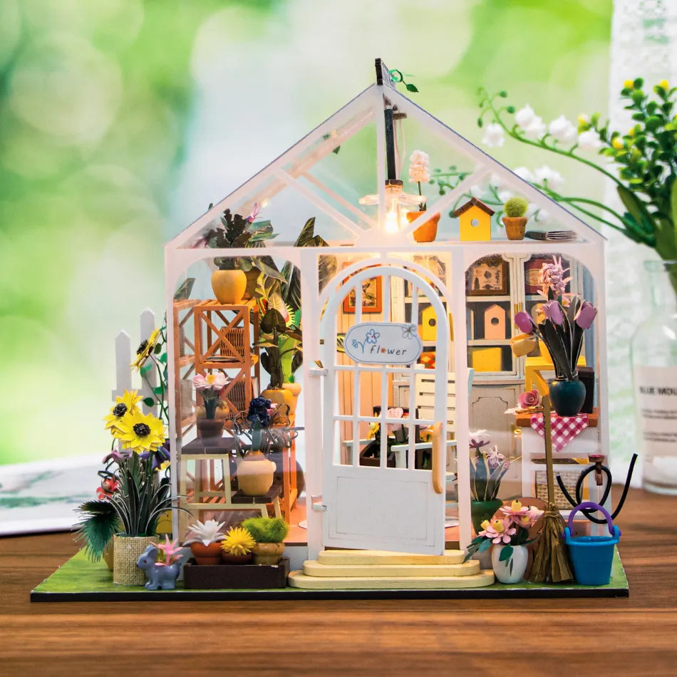 Miniature model of a greenhouse with plants and decor on a wooden surface.