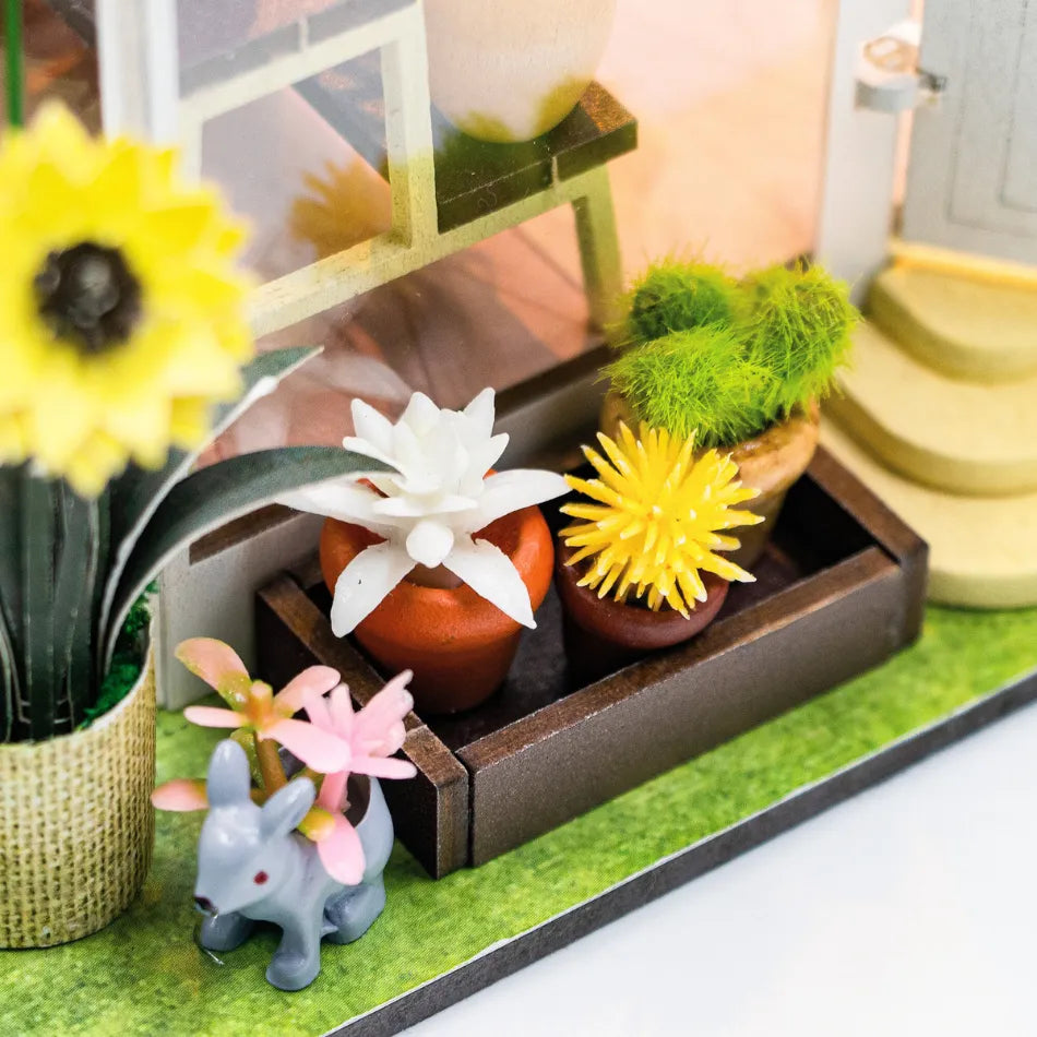 Miniature garden setup with flowers and a small rabbit figurine on a green surface.