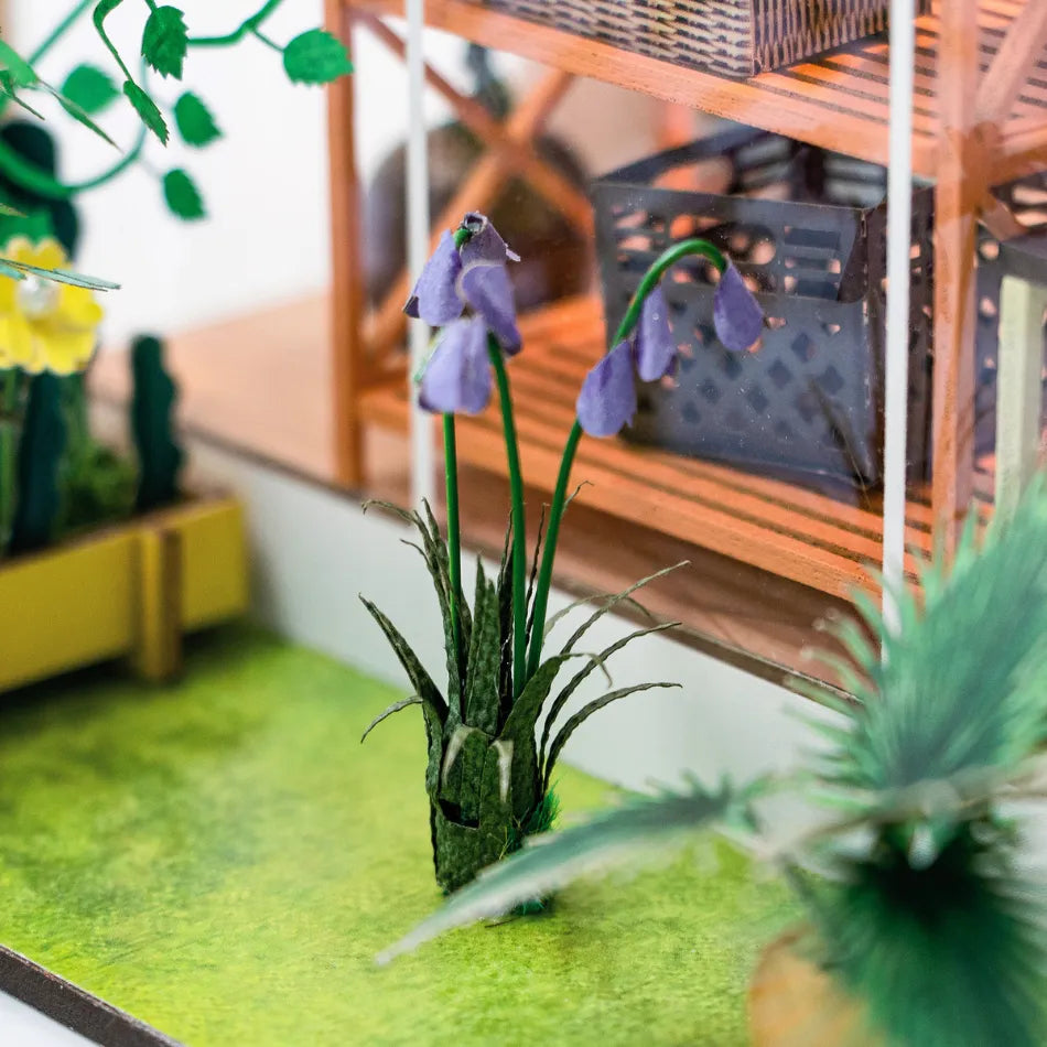 Miniature garden scene with purple flowers and green plants on a grassy surface.