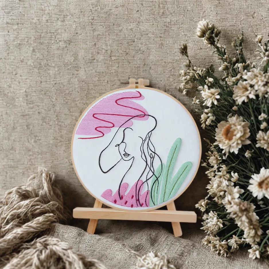 Embroidery hoop with a woman's face design on a textured surface with flowers.