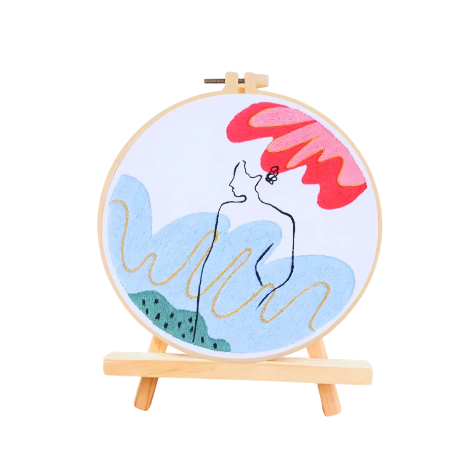 Embroidery hoop with a colorful design of a woman and flamingo on a white background