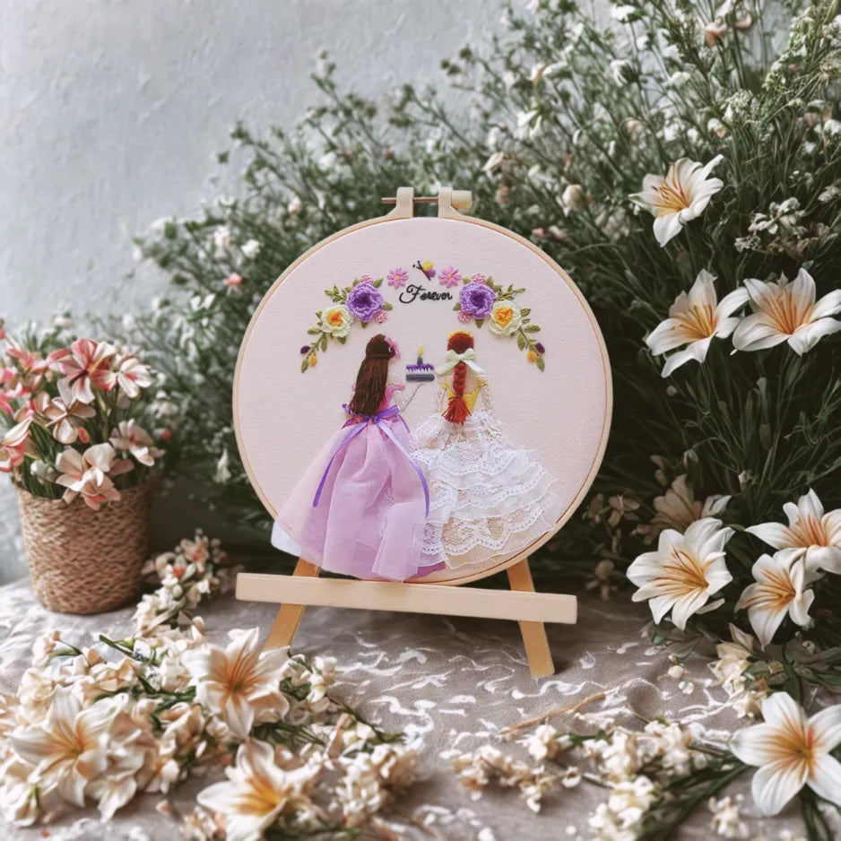 Embroidery hoop with a couple design surrounded by flowers on a table.