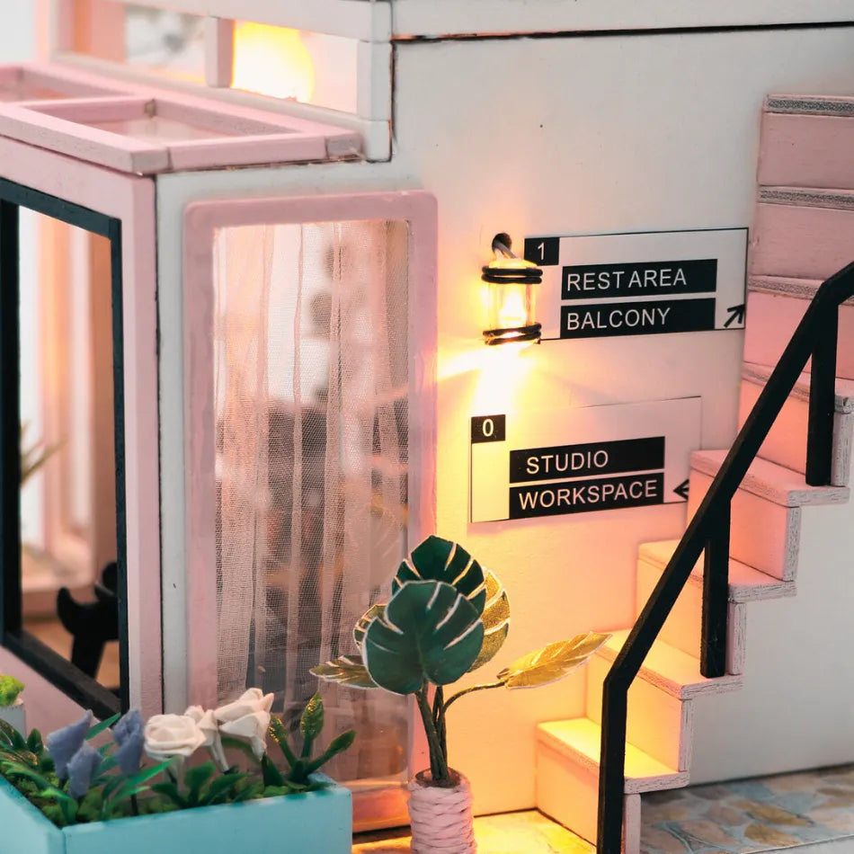 Miniature studio with pink staircase, plant, and sign indicating 'Studio Workspace'.