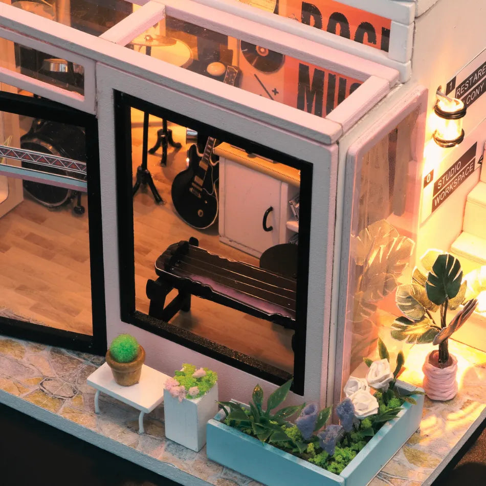 Miniature room model with furniture and decor, including a guitar and plants.