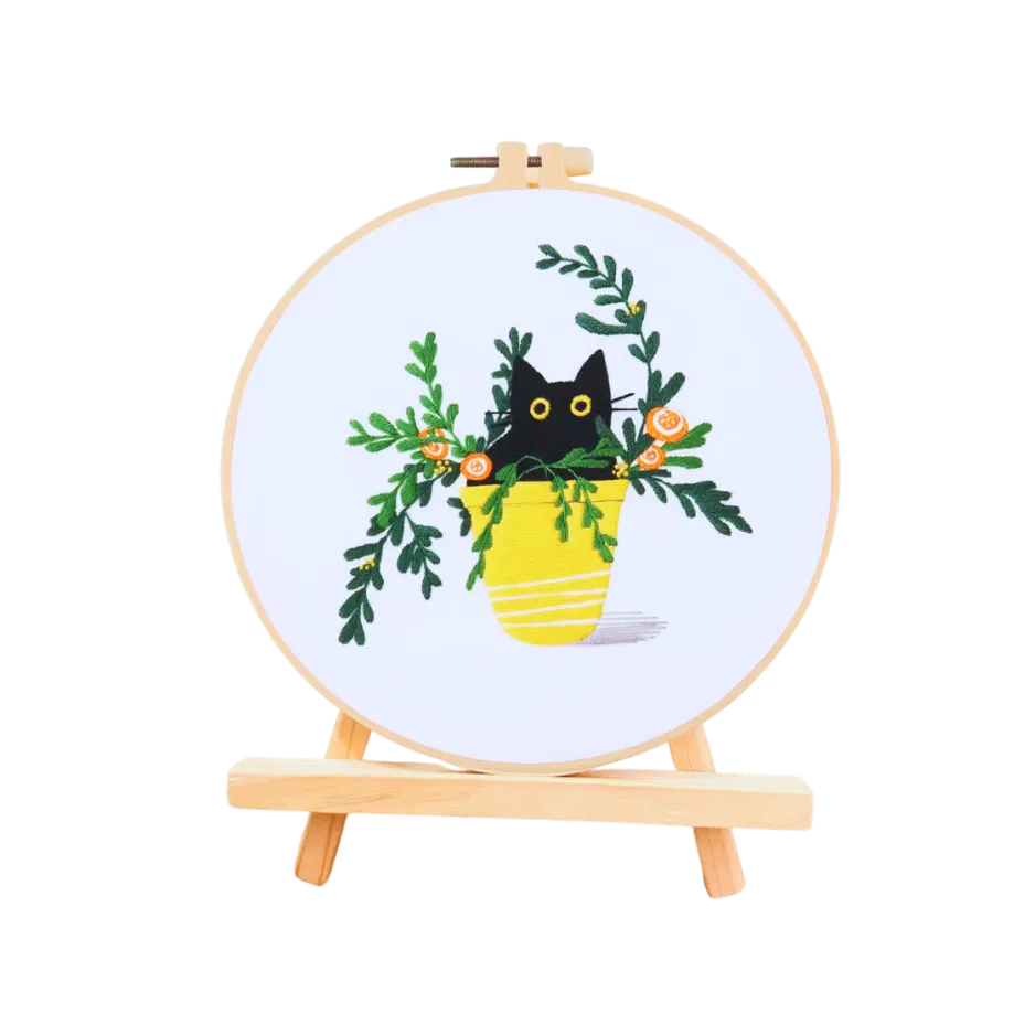 Embroidery hoop with a black cat in a yellow pot and green leaves design on a white background
