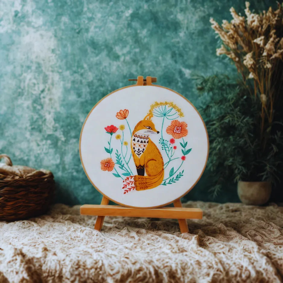 Embroidery hoop with a fox design on a textured surface with plants in the background