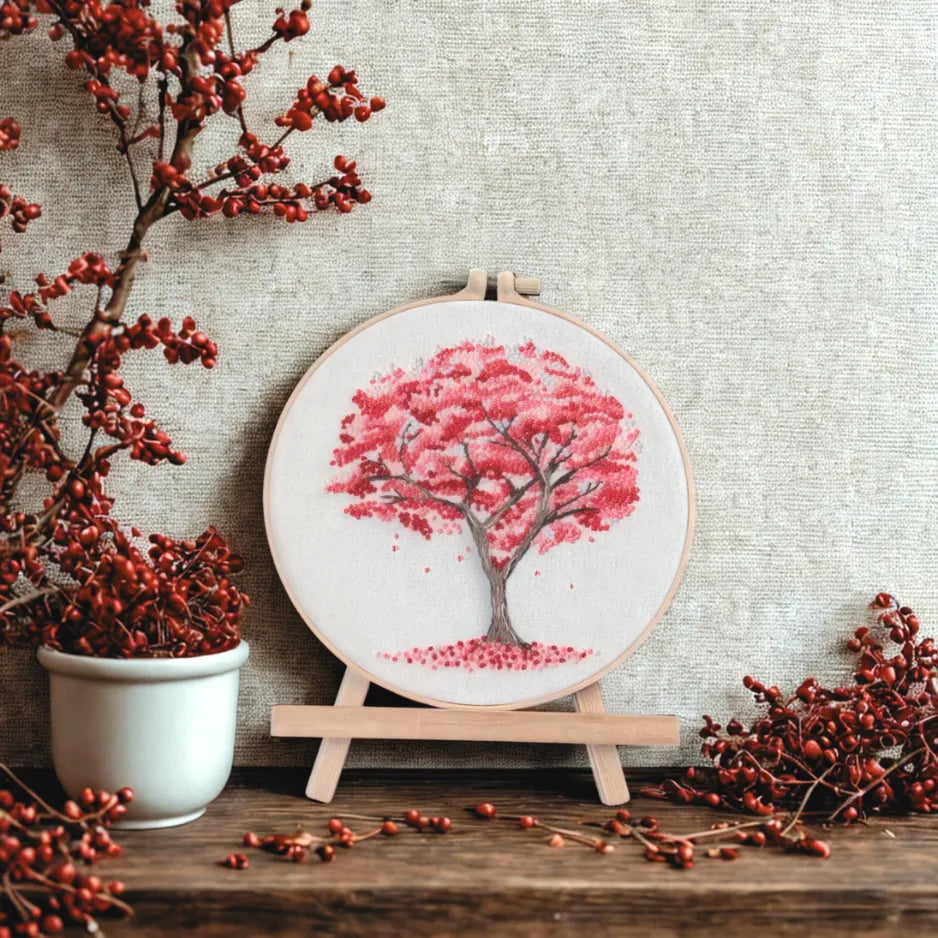 Embroidery hoop with pink tree design on a wooden surface with red berries.