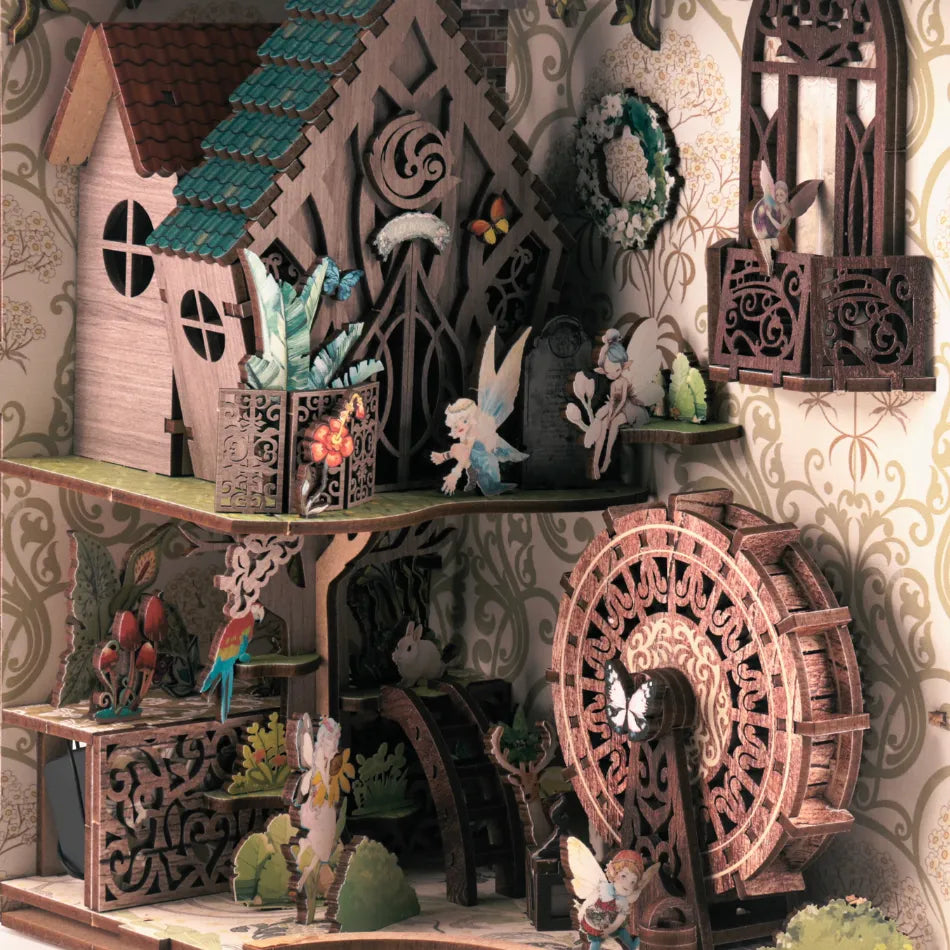 Miniature fairy garden scene with a house, water wheel, and various fairy figures on a decorative background.