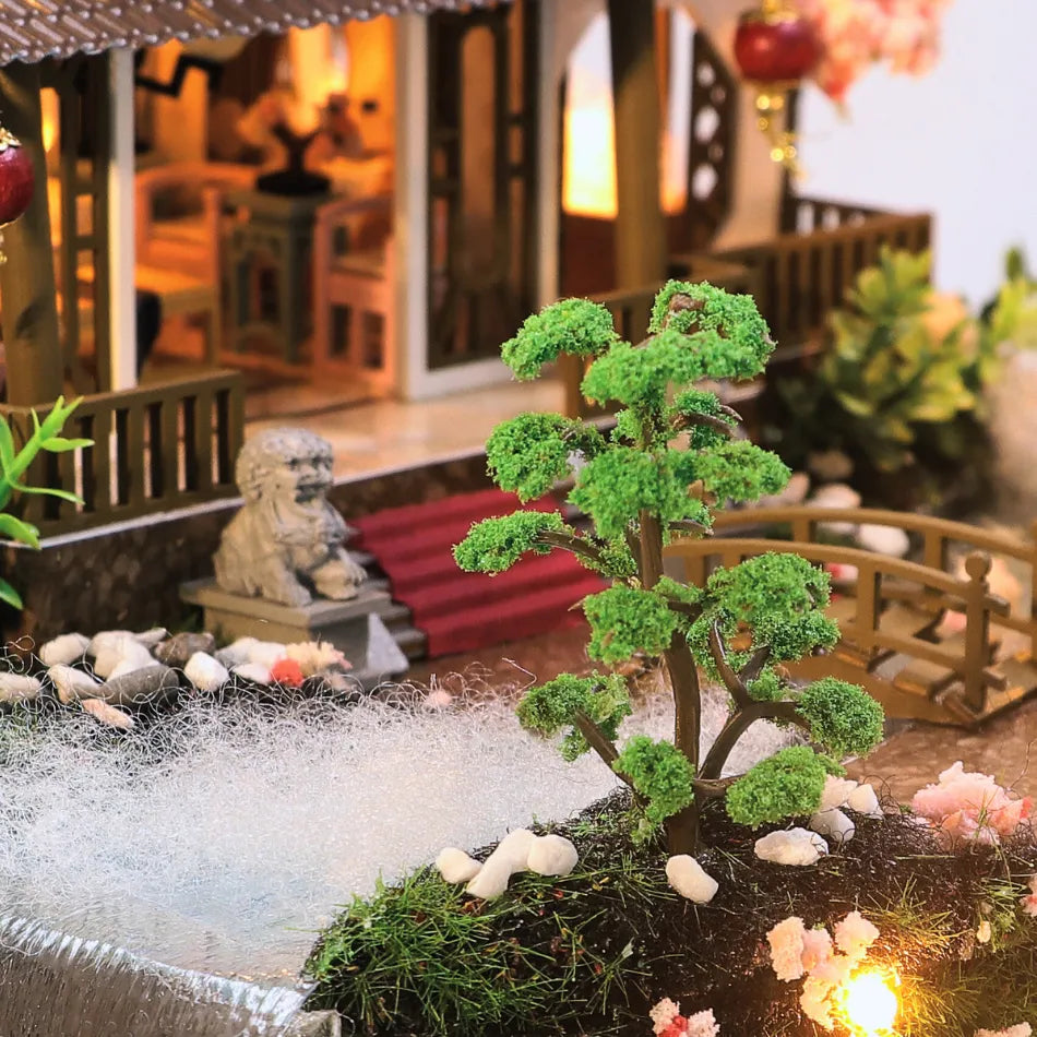 Miniature garden scene with a tree, rocks, and a small bridge in a decorative setting.