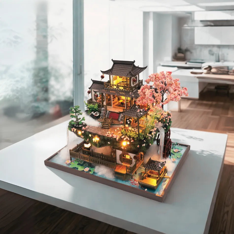 DIY miniature Asian-style watermill house with warm lights, cherry blossom tree, waterfall, and wooden bridges — detailed craft model kit on a transparent background.