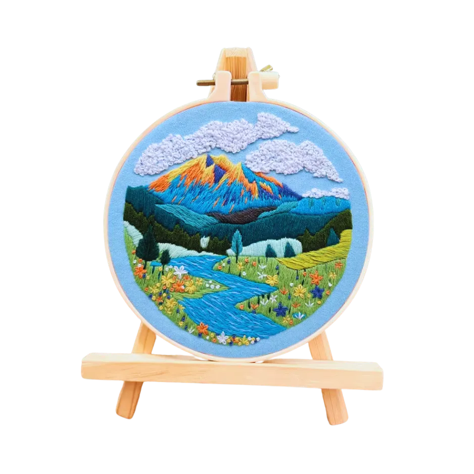 Embroidery of a mountain landscape on a round hoop with a wooden stand against a white background