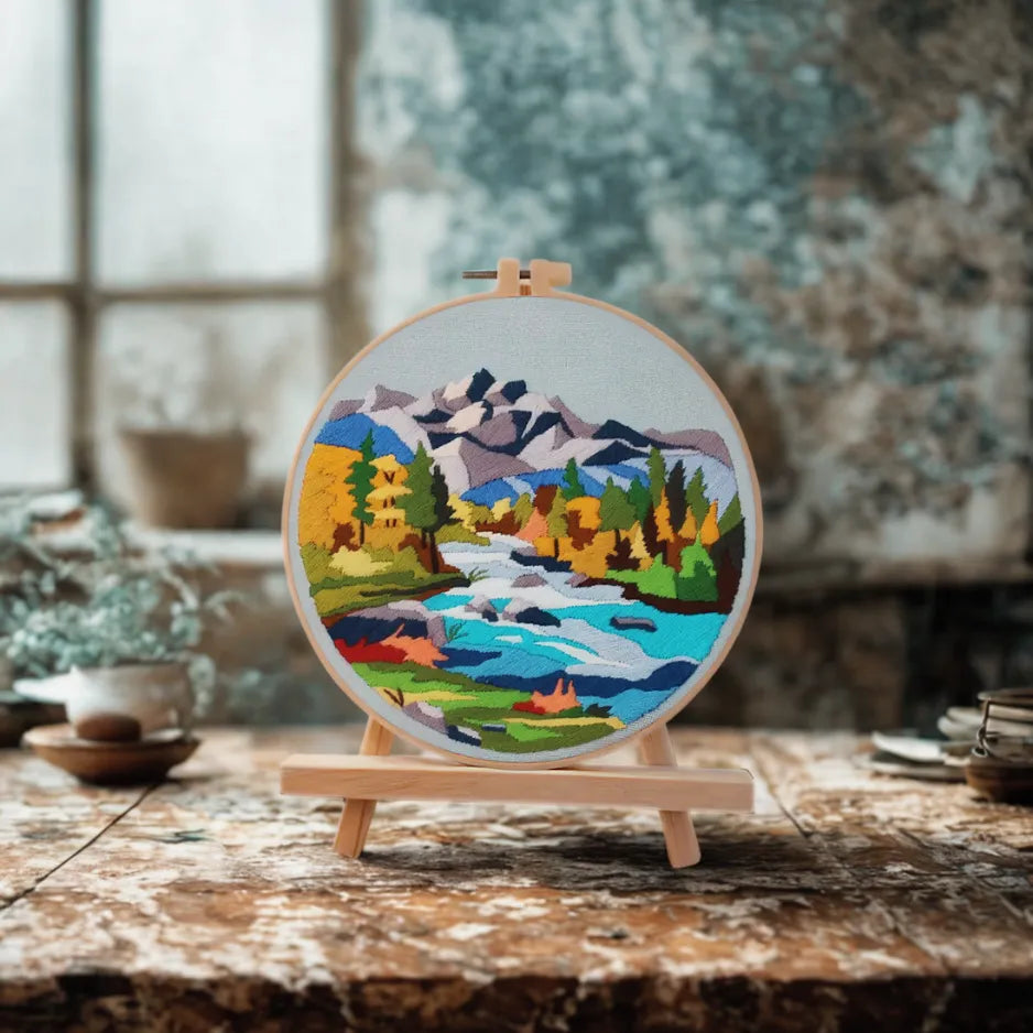 Embroidery hoop with a colorful landscape design on a wooden table.