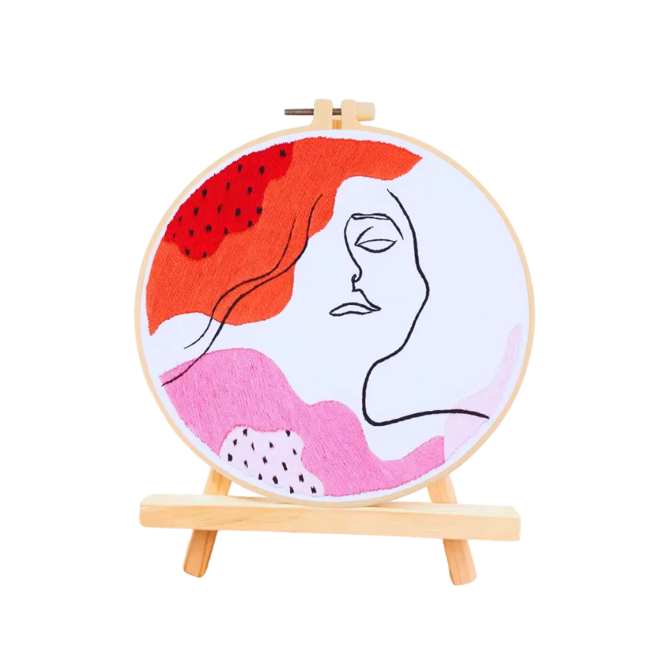 Embroidery hoop with abstract design of a face and red and pink shapes on a white background